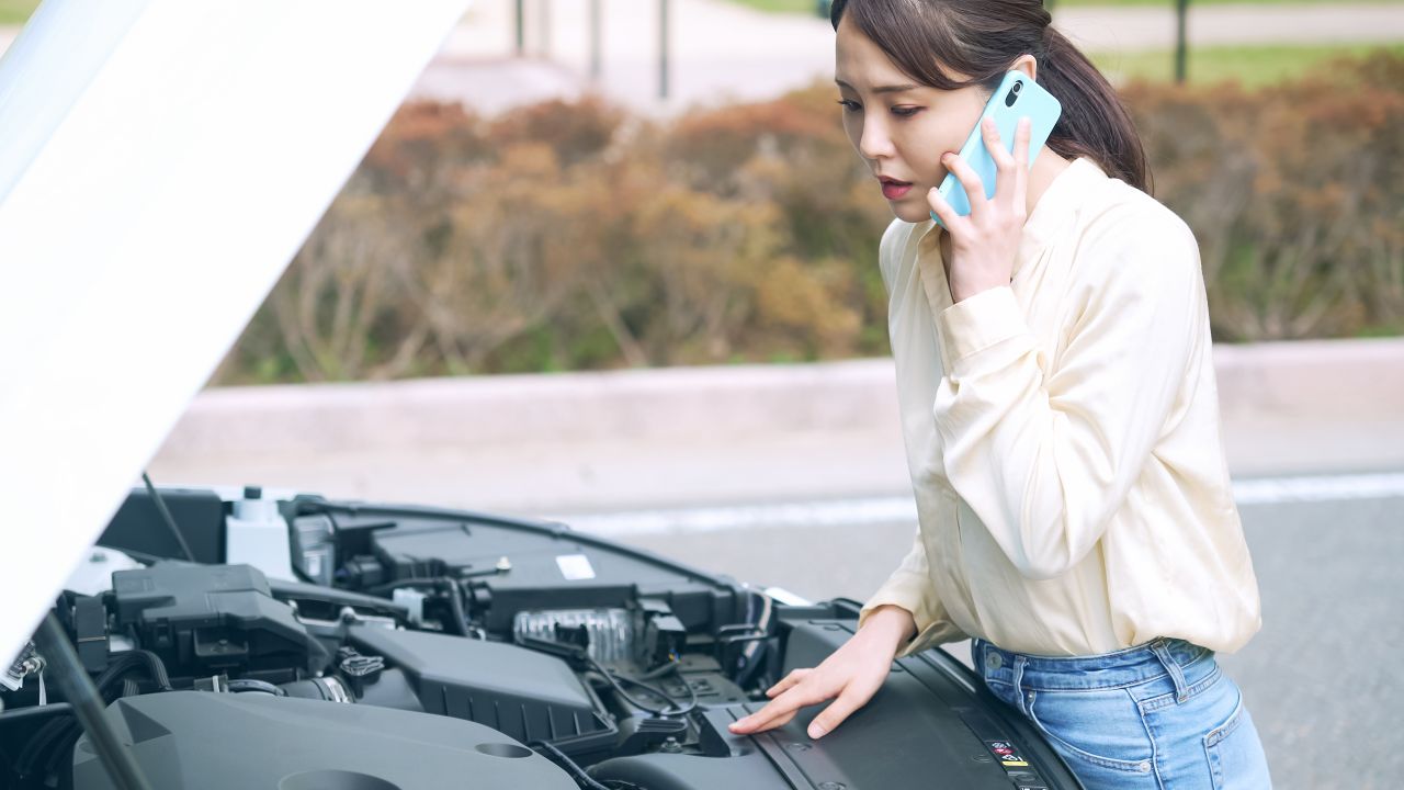 車のエンジンルームを見つめながら電話している女性